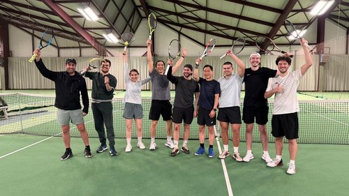 Gruppe von jungen Menschen die vor dem Tennisnetz ihre Schläger hochhält
